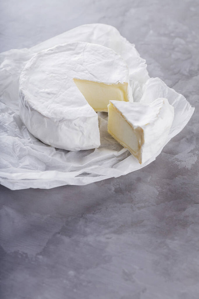 Camembert on a gray cement background. Soft cheese with white mold on parchment paper. Copy space. Top view - Фото, зображення