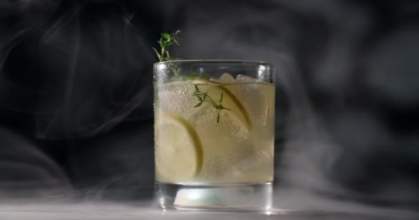 Koud glas met cocktail draait langzaam in de rook op de donkere achtergrond, alcoholische dranken en dranken, alcoholvrije cocktail, objectvideo van limonade, 4k Prores HQ - Video