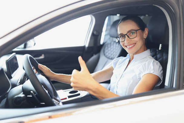 Portrait of smiling woman driving new car shows thumbs up closeup - 写真・画像