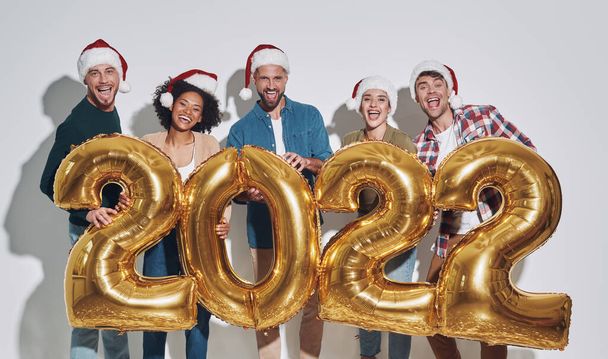 Group of young beautiful people in Christmas hats carrying gold colored numbers and smiling - Фото, зображення