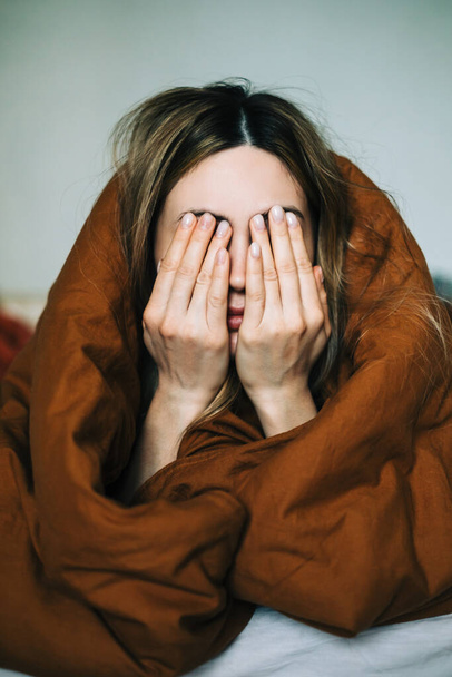Young caucasian woman waking up in the morning, lying under cover and rubbing face. - Foto, afbeelding