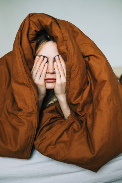 Jeune femme caucasienne se réveillant le matin, couchée sous couverture et frottant le visage. - Photo, image