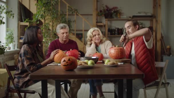 Young man shows his grandparents and african american woman how to cut a pumpkin for Halloween - Footage, Video