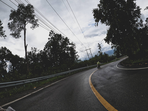 Vista durante la guida di una moto su una strada di montagna nella foresta pluviale nella stagione delle piogge. Motociclista sta guidando una moto sulla strada. - Foto, immagini