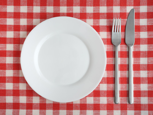 Plate with fork and knife on a red checkered tablecloth. - Фото, зображення