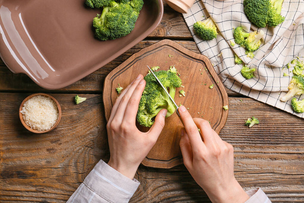 Woman cutting healthy broccoli cabbage on wooden background - Fotoğraf, Görsel