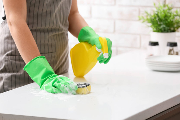 Woman cleaning table with sponge and detergent in kitchen - Foto, afbeelding