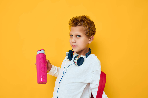 elegante niño auriculares entretenimiento agua botella amarillo fondo - Foto, imagen