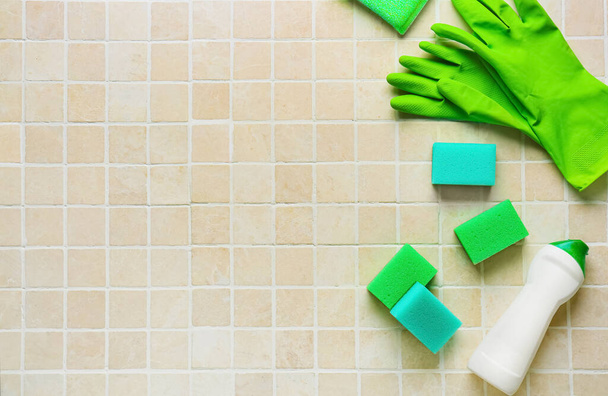 Groene reinigingssponzen, handschoenen en fles wasmiddel op tegelondergrond - Foto, afbeelding