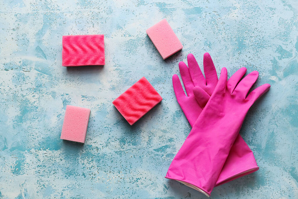 Roze schoonmaak sponzen en handschoenen op grunge kleur achtergrond - Foto, afbeelding