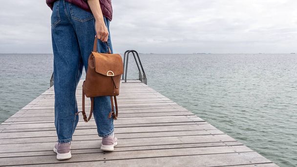 Chica joven con una mochila, mira al mar, en un muelle de madera. Primer plano. Libertad. Viajes. Estilo de vida. - Foto, Imagen