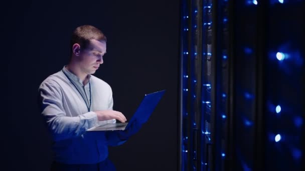 IT technician in data center digital server room controlling work of rack server cabinets with a tablet. Professional server engineer at work. Man technicians working in high tech server rack room - Footage, Video