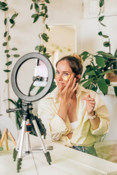 Young woman beauty blogger broadcasts live streaming to review makeup and cosmetic products on social media,applies patches under the eyes.Beauty and technology concept.Selective focus. - Фото, зображення