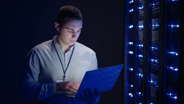 IT technician in data center digital server room controlling work of rack server cabinets with a tablet. Professional server engineer at work. Man technicians working in high tech server rack room - Footage, Video