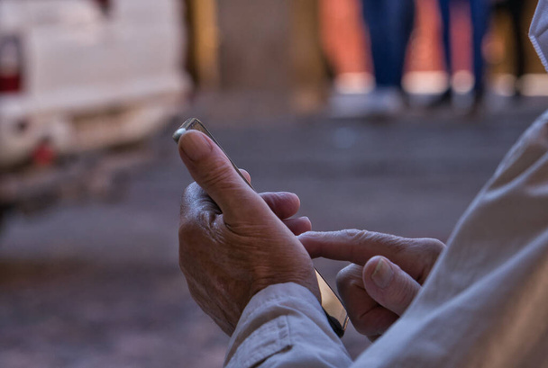 Detalle de cerca de la mano de un anciano usando su teléfono móvil en la calle. Concepto de uso de la tecnología por los ancianos. Hombre mayor usando tecnología. - Foto, imagen