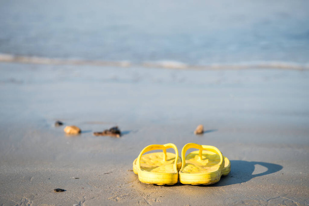Keltaiset varvastossut tai kumitossut rannalla liikeaallolla Ao Nangissa, Krabissa, Thaimaassa. sandaalit hiekalla hauskaa loma matka käsite kesäaikaan aurinkoisena päivänä. Kesäloma vibes. - Valokuva, kuva