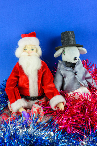Santa Claus and a rat wrapped in tinsel on a blue background. Christmas and New Year concept. - Photo, Image