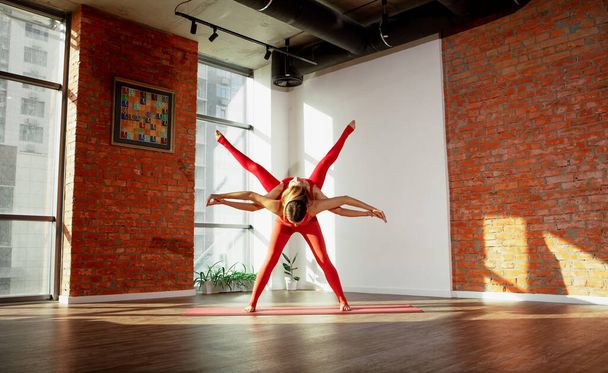 Paarweise Yoga-Asana. Junge Mädchen in Sportuniformen tun schöne Paar Asana in geräumigen Yoga-Studio - Foto, Bild