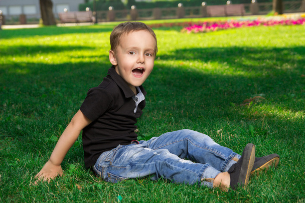 Kleiner Junge öffnete den Mund weit, während er auf dem Gras saß  - Foto, Bild