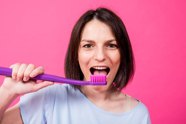 Beautiful happy young woman with big toothbrush on blank pink background - Zdjęcie, obraz