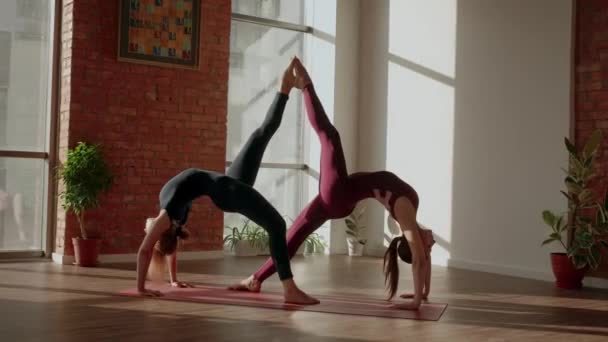 Young womans doing beautiful pair asana Eka pada urdhva dhanurasana in a spacious yoga studio - Footage, Video