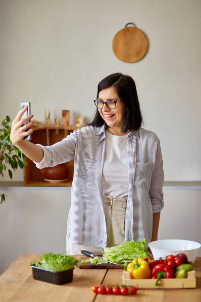 Mujer tomando selfie o hace una lección de video sobre cocinar, en el teléfono celular, teléfono inteligente para su blog en la cocina en casa, concepto de blogger de alimentos, estilo de vida saludable. Transmisión en línea - Foto, imagen
