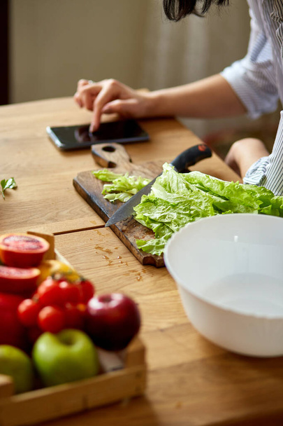女性は自宅でキッチンで料理をしています,デジタルタブレットやスマートフォンを使用して,レシピを探して,健康食品のコンセプト,ビーガンや食事. - 写真・画像