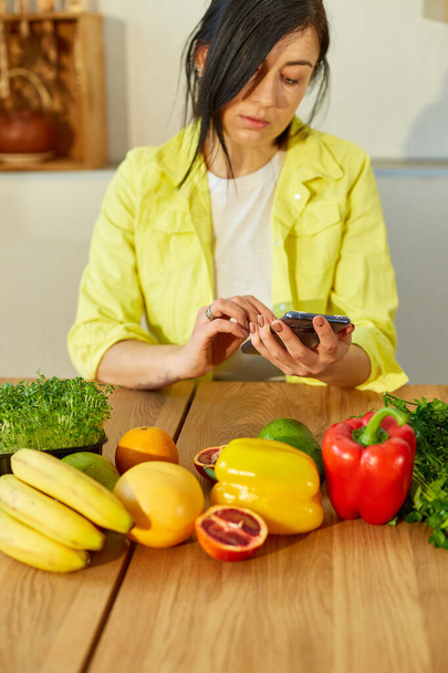 Жінка використовує цифровий планшет або смартфон, шукаючи рецепт приготування їжі на кухні вдома, концепцію здорової їжі, веганську або дієту. Продуктові інтернет-магазини
 - Фото, зображення