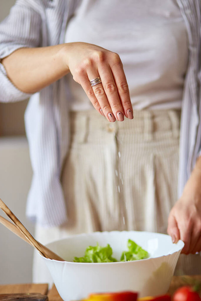 Donna sta preparando insalata di verdure in cucina, mescolando foglia di insalata e verdure in ciotola bianca, concetto di cibo sano, vegan o dieta. - Foto, immagini