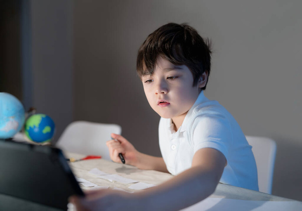 School kid using tablet for his homework,Child boy doing homework by using digital tablet searching information on internet after back from school,E-learning, Home schooling education concept - Photo, Image