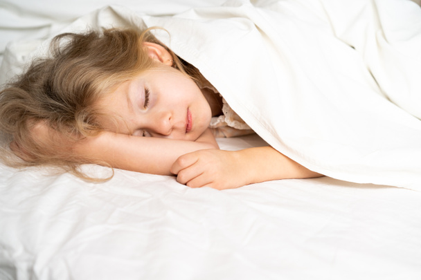 Маленькая блондинка сладко спит в кровати с белым нижним бельем. место для текста. здоровый сон ребенка. - Фото, изображение
