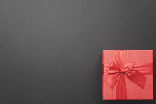 Caja de regalo roja con un arco en la esquina sobre un fondo gris oscuro. Vista superior. tarjeta de felicitación - Foto, Imagen