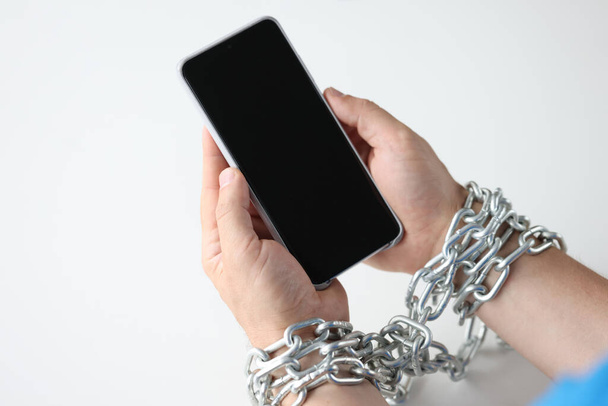 Руки завернуты в цепь держать черный смартфон крупным планом - Фото, изображение