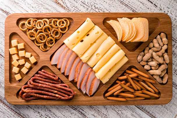 wooden tray with meat and cheese, antipasto snacks. Antipasto cold meat dish with breadsticks, prosciutto, ham, ham slices and cheese on a wooden tray top view, flat lay - Foto, immagini