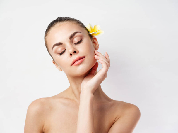 mujer bonita sosteniendo la mano cerca de la cara hombros desnudos piel clara flor amarilla - Foto, imagen