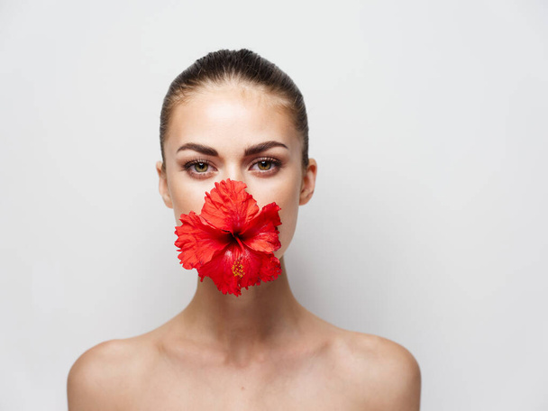 Ağzında kırmızı çiçekli güzel bir kadın çıplak omuzları kozmetik. - Fotoğraf, Görsel