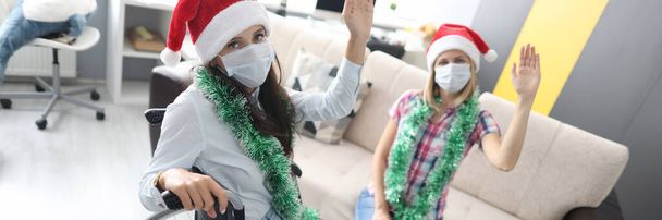 Disabled woman in wheelchair and friend in medical mask greeting christmas at home and waving - Φωτογραφία, εικόνα