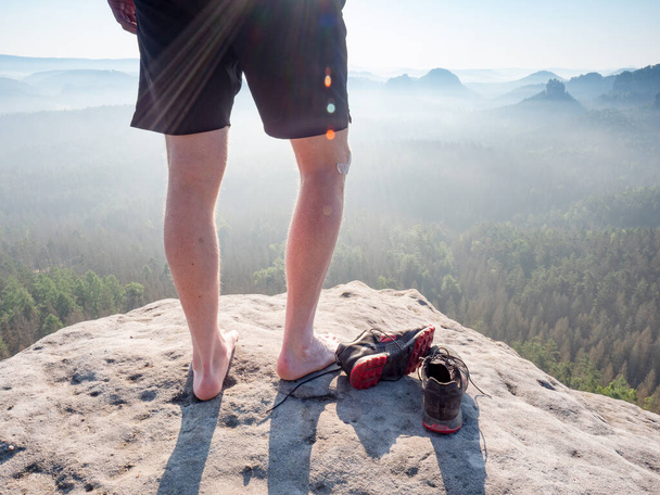 Среднего возраста здоровое мужское тело с голыми ногами на горной вершине скалы. Любители путешествий наслаждаются видом. Высокий человек на скалистой скале смотрит на пейзаж.  - Фото, изображение