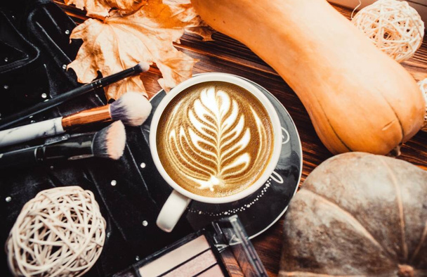 Taza de café, sombra de ojos, pinceles de maquillaje sobre fondo marrón madera con calabazas - Foto, Imagen