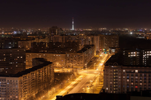 Повітряна нічна фотографія вулиці з освітленими ліхтарями і високими житловими будинками. Ілюмінована телевізійна вежа на фоні. Концепція життя великого міста
. - Фото, зображення