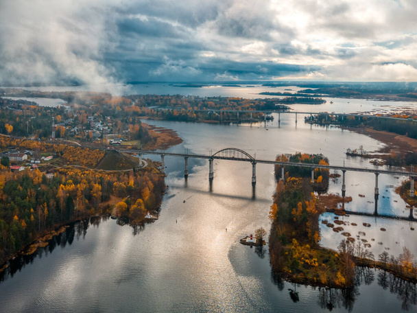 Foto aérea da antiga ponte suspensa ferroviária acima do rio. Paisagem de outono com a natureza do norte. Árvores com folhas amarelas e laranja no fundo. Céu nublado. Conceito de transporte. - Foto, Imagem