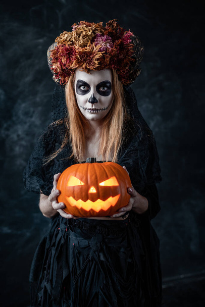 a woman in the image of a witch holds a Halloween pumpkin with a lantern - Photo, Image