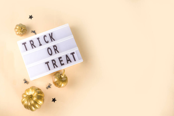Trick or treat background, Simple Halloween greeting card, party invitation abstract flatlay with golden colored pumpkins, stars, spiders, on beige yellow background copy space top view - Photo, image