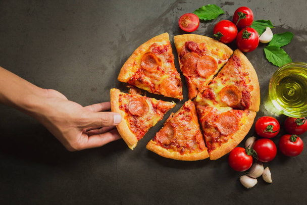 Bovenaanzicht van hete pepperoni pizza, Lekkere pepperoni pizza en koken ingrediënten tomaten basilicum op zwarte achtergrond. - Foto, afbeelding
