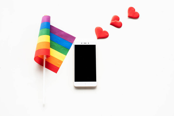 Bracelets arc-en-ciel LGBT symbole de fierté avec smartphone sur fond blanc. Liberté amour, liberté de parole, rencontres en ligne, rencontre en ligne, félicitations, souhaits sur smartphone, bavardage. - Photo, image