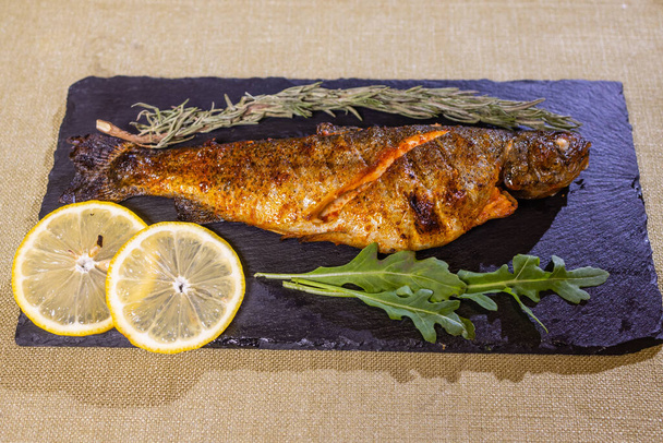 Roasted gilthead fishes with lemon, herbs, salt on black background. Healthy food concept. Food frame. - 写真・画像