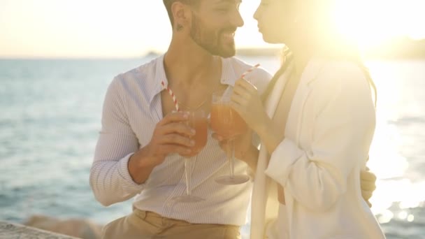 Χαμογελαστό ζευγάρι ισπανόφωνων με κοκτέιλ που φιλιούνται στη θάλασσα - Πλάνα, βίντεο