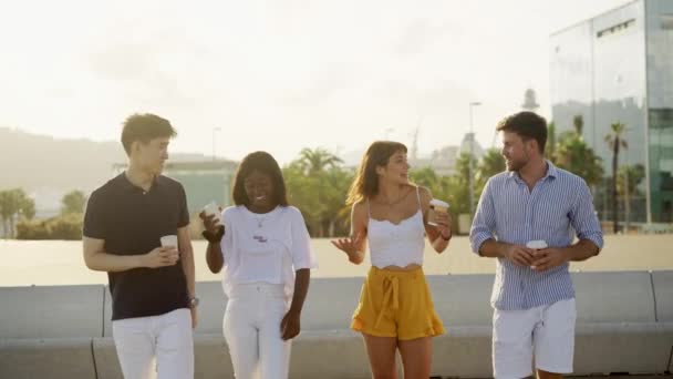 Neljä nuorta hymyilevää monikansaista ystävää juomassa vie kahvin ja juttelemassa ulkona - Materiaali, video