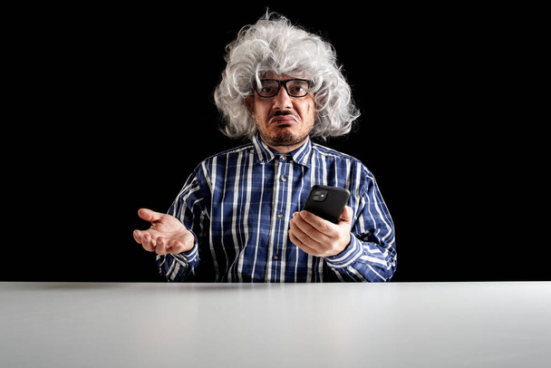 A bewildered senior, typical boomer,  does not understand how to use the smartphone on black background - Photo, Image