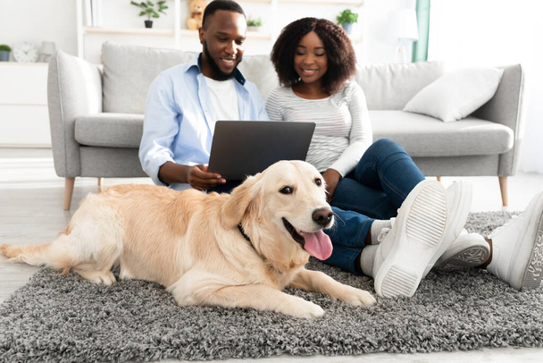 Μαύρο ζευγάρι στο σπίτι χρησιμοποιώντας φορητό υπολογιστή χαλαρώνοντας με το σκυλί - Φωτογραφία, εικόνα
